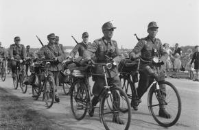 Militairen, lopend naast hun fietsen, gaan hun wapens en uitrusting inleveren na de Bevrijding