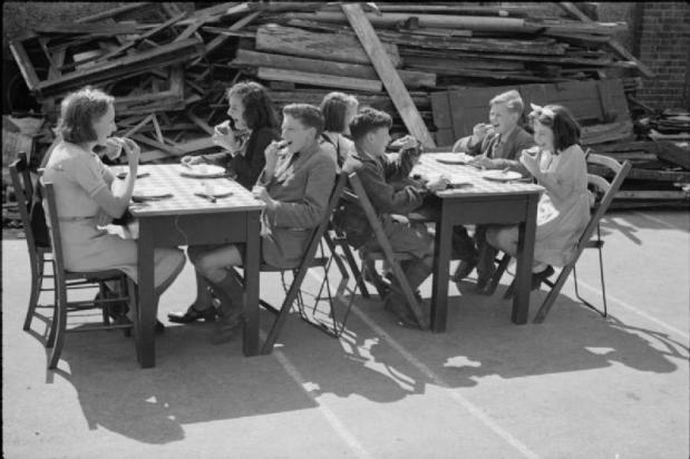 Schoolkinderen eten Amerikaans voedsel, verkregen via de Lend-Lease act, op het speelplein van hun gebombardeerde school, London